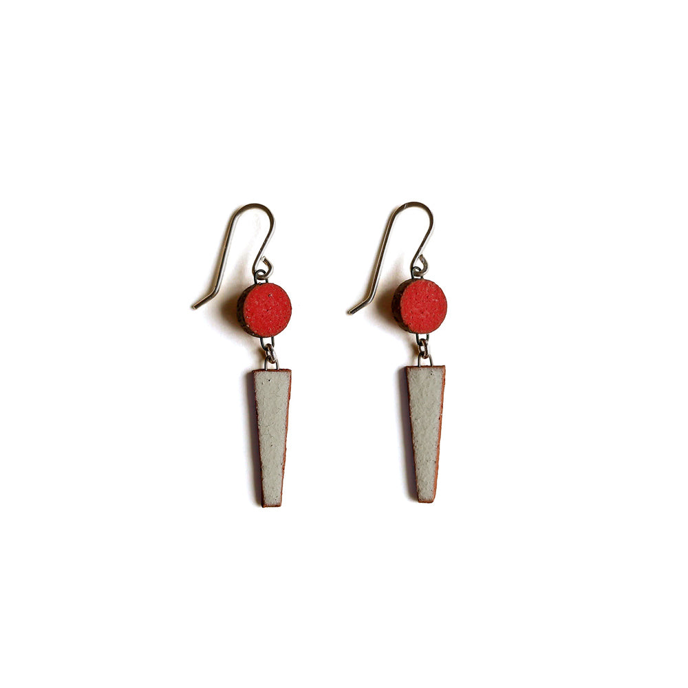 Pair of earrings with red circular tops and triangular bottoms on a white background