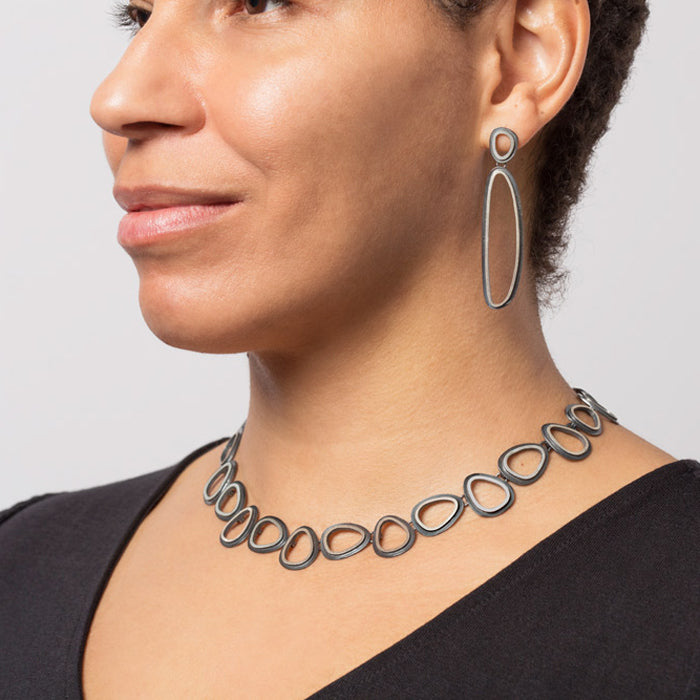 Woman wearing a silver necklace and earrings on a plain background