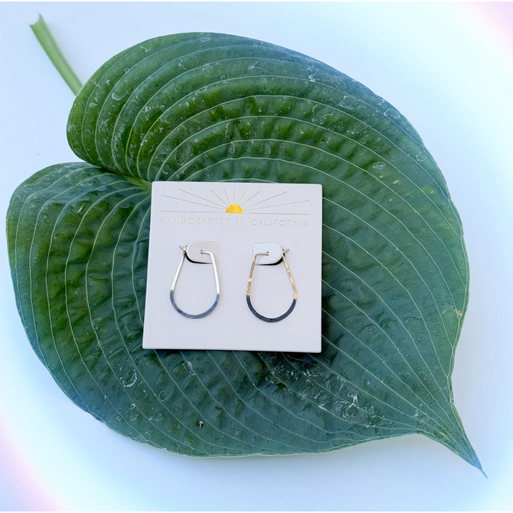 Pair of hoop earrings on a white card with a yellow sun design, placed on a large green leaf.