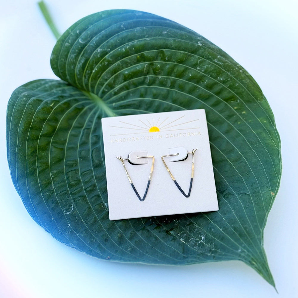 Pair of earrings on a white card with a yellow sun design, placed on a large green leaf.