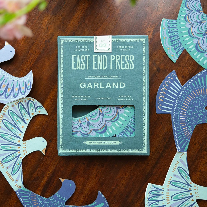 A close-up of decorative bird cutouts arranged in a row on a white background. The birds are stylized with intricate geometric and scalloped patterns in shades of blue, teal, with gold accents.
