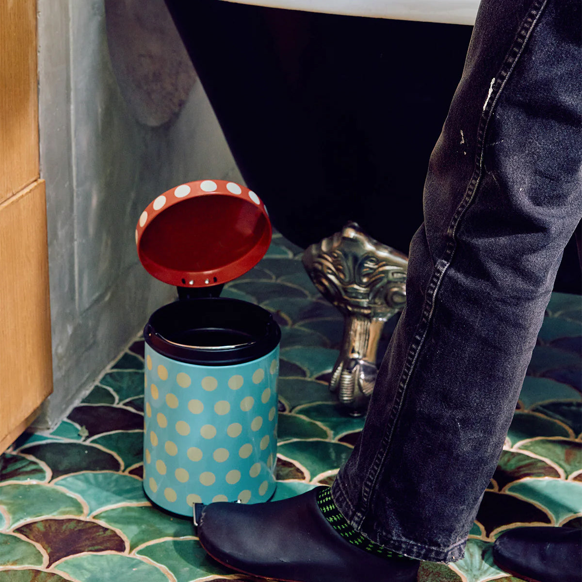 Person using a small polka dot trash can on a tiled bathroom floor.