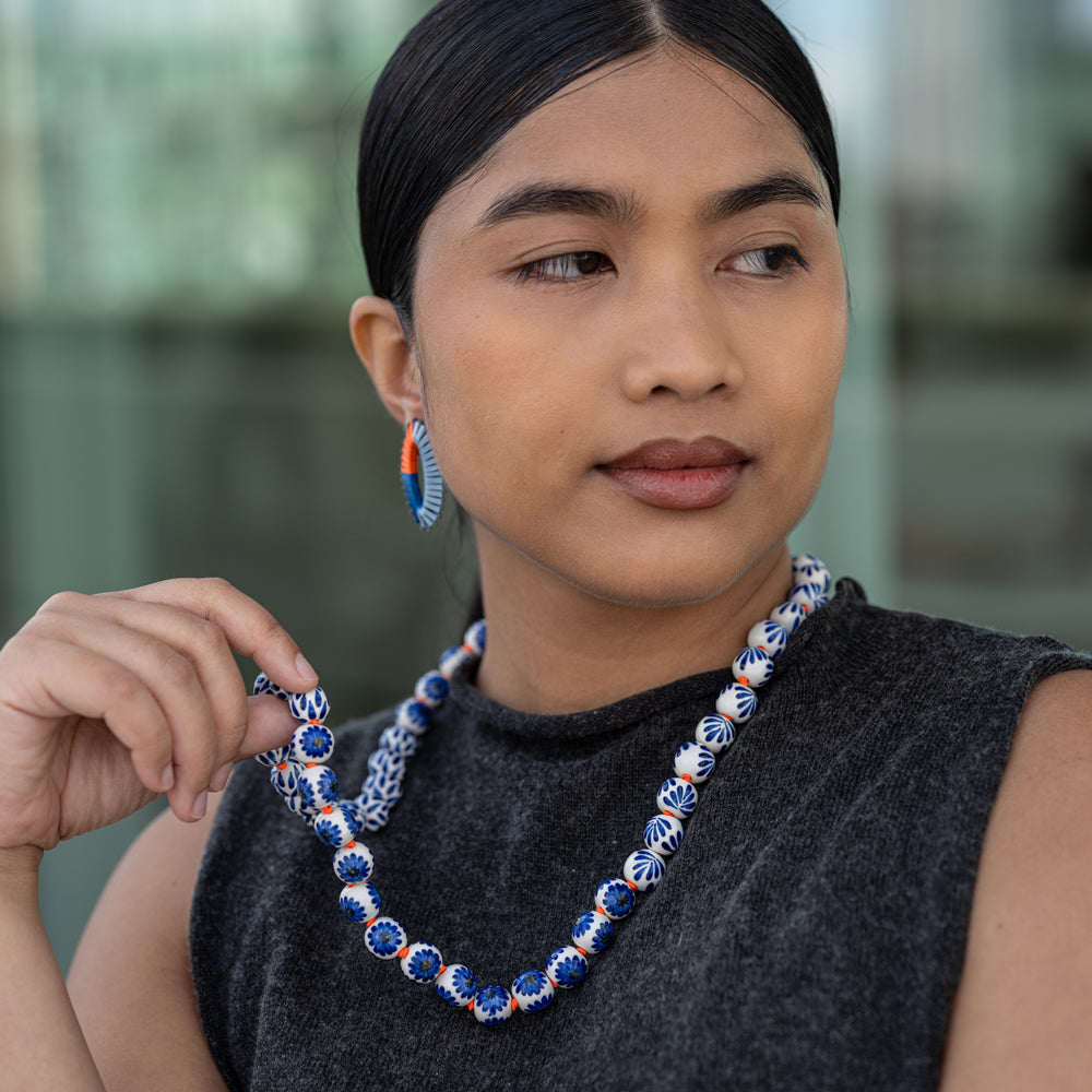 Woman wearing a long blue and orange beaded necklace with a blurred background