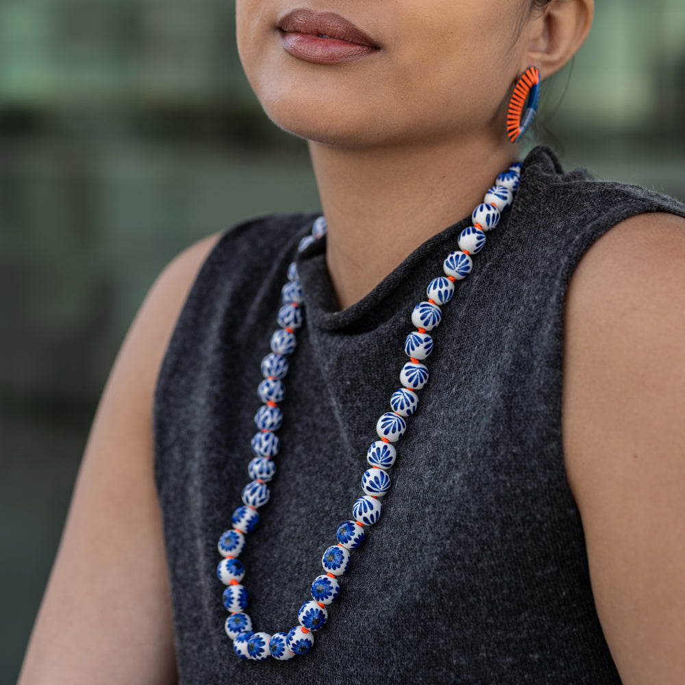 Woman wearing a long blue and orange beaded necklace with a blurred background