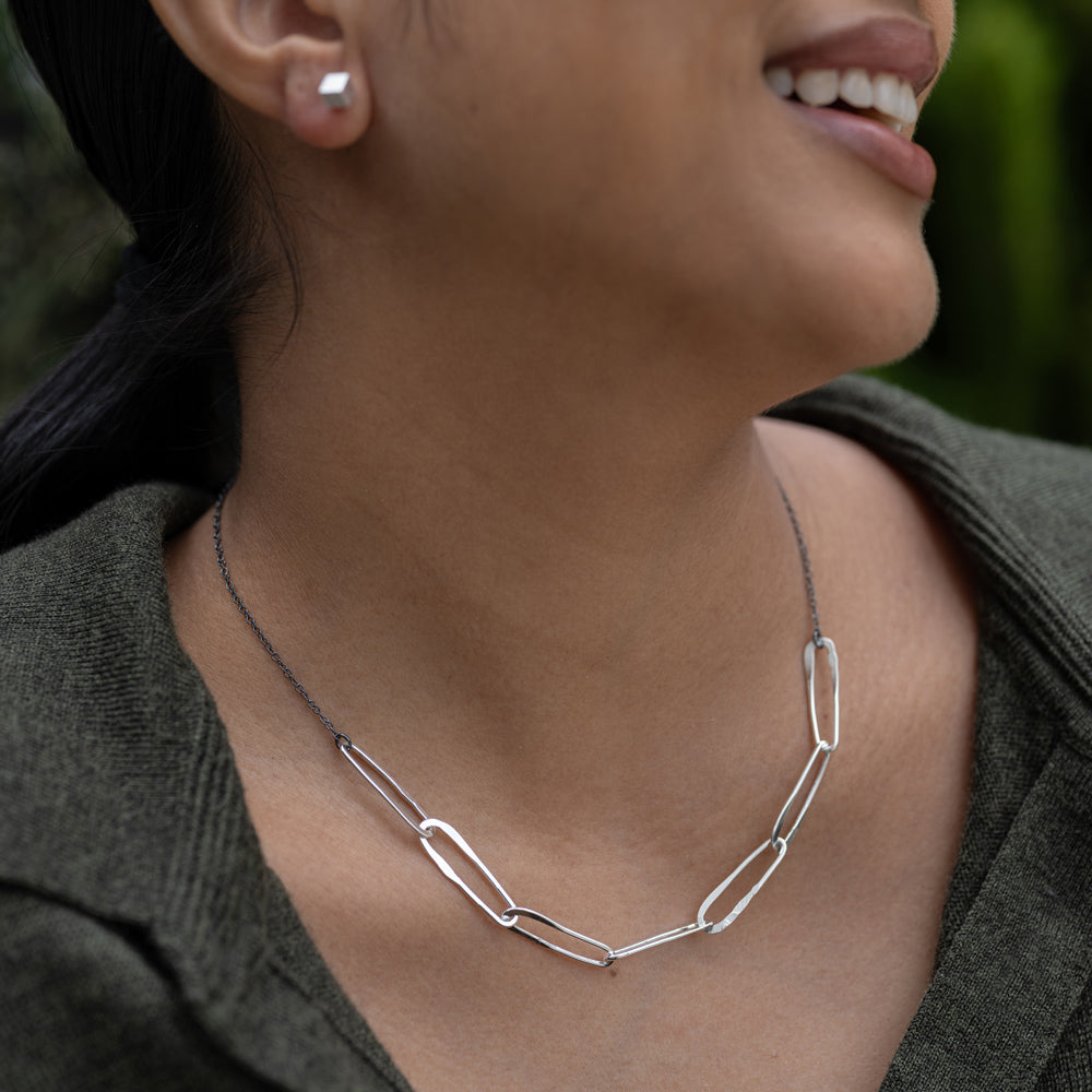 Close-up of a person wearing a silver necklace with a blurred background