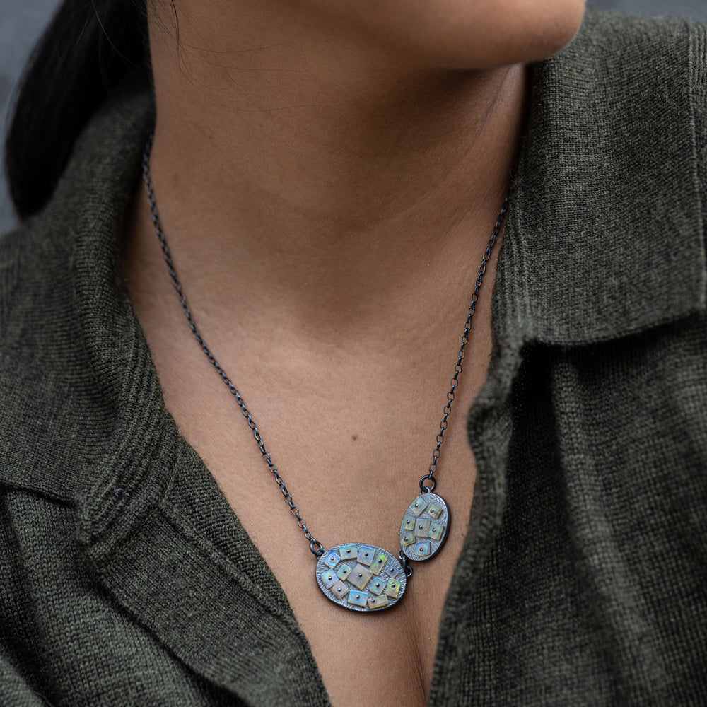 Necklace with two pendants worn by a person in a dark green shirt.