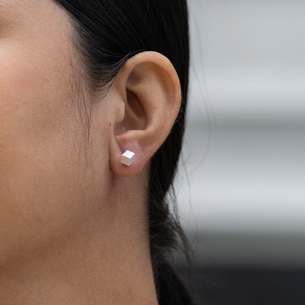 Close-up of an ear wearing a silver stud earring with a blurred background