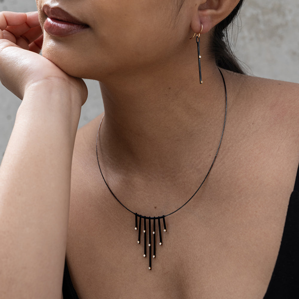 Woman wearing a black fringe necklace and earring set against a neutral background