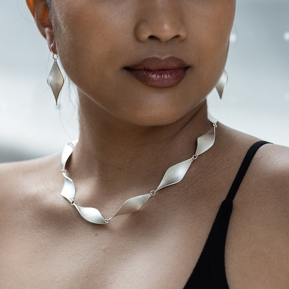 Close-up of a person wearing a silver necklace with a blurred background