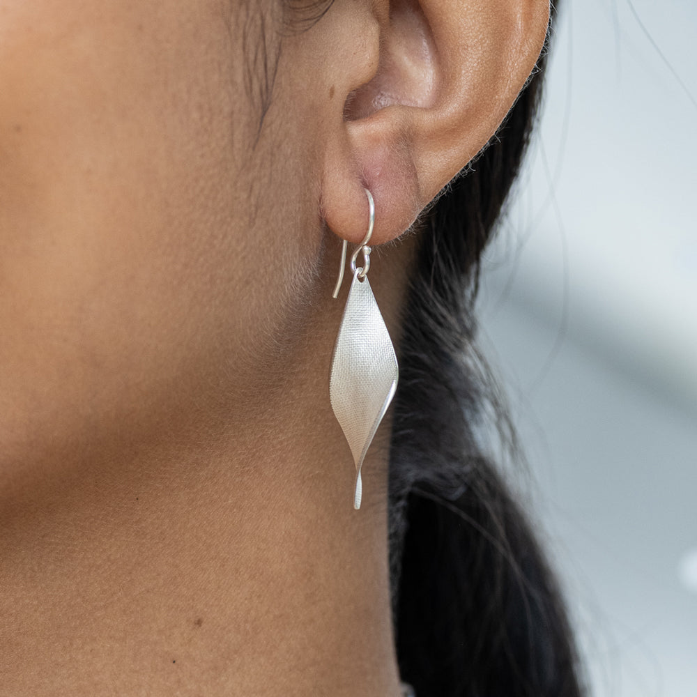 Silver teardrop earring worn by a person with a blurred background