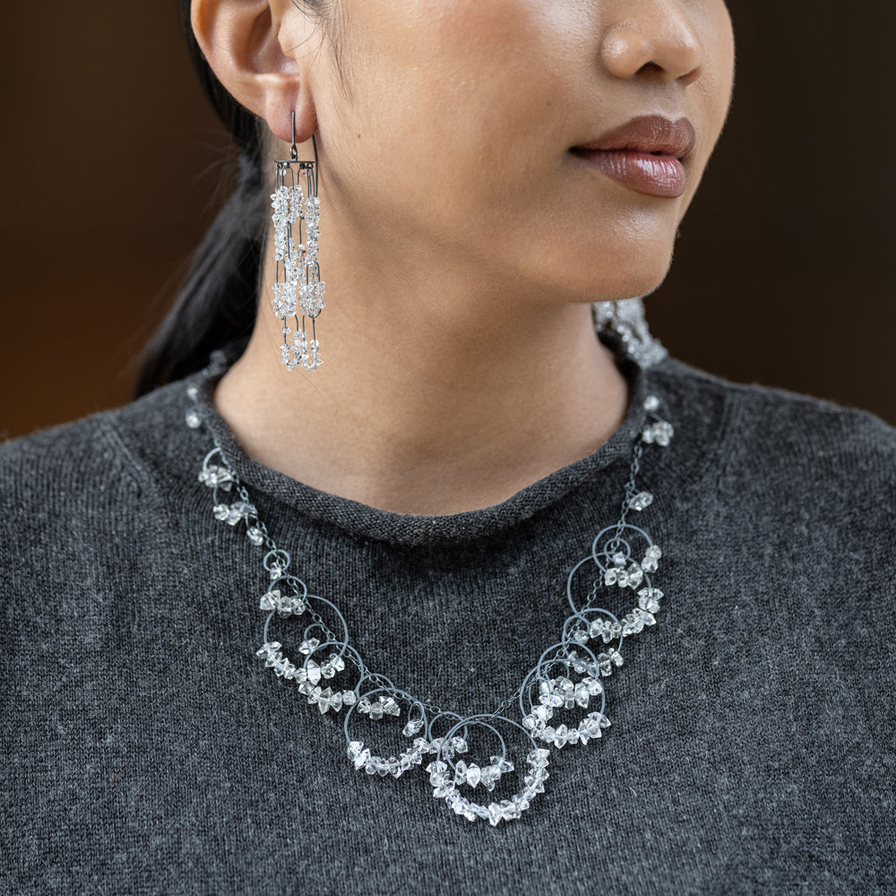 Close-up of a woman wearing a necklace and earrings against a dark background