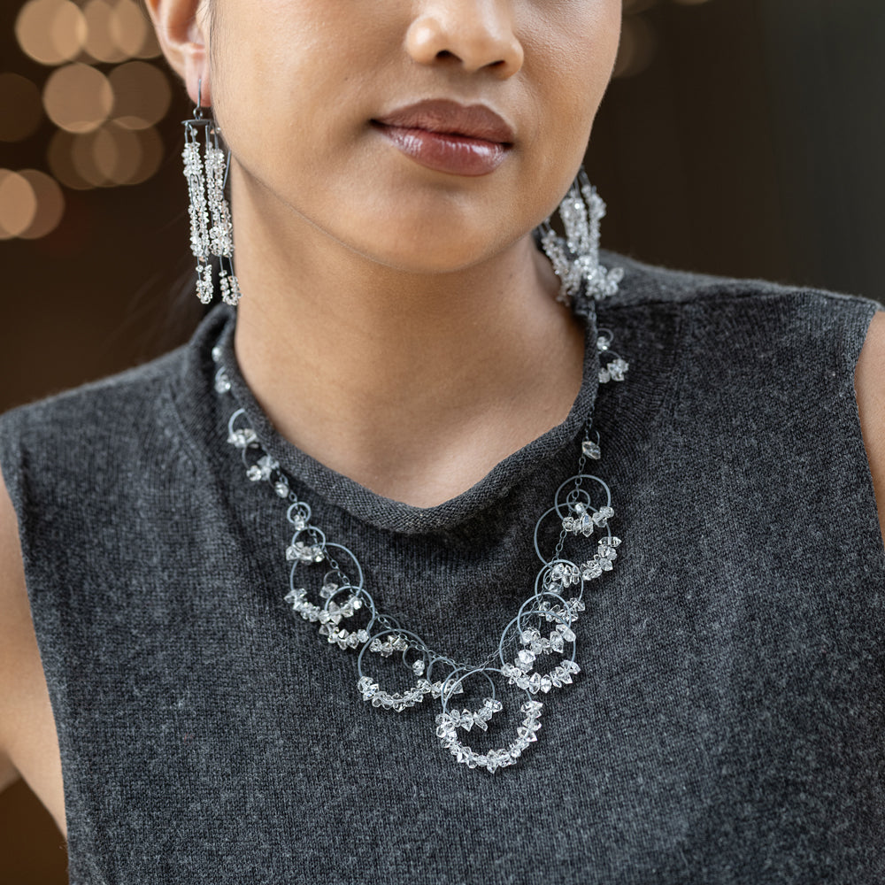 Woman wearing a Herkimer Quartz necklace and earrings with a blurred background