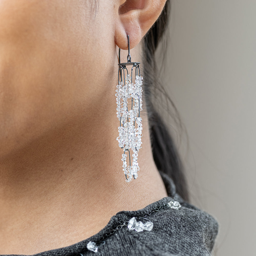Close-up of a person wearing sparkling silver earrings with a neutral background