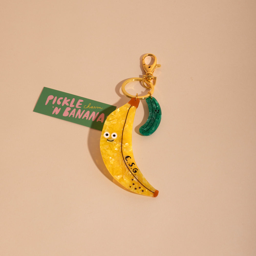 Banana-shaped keychain with a pickle on a beige background