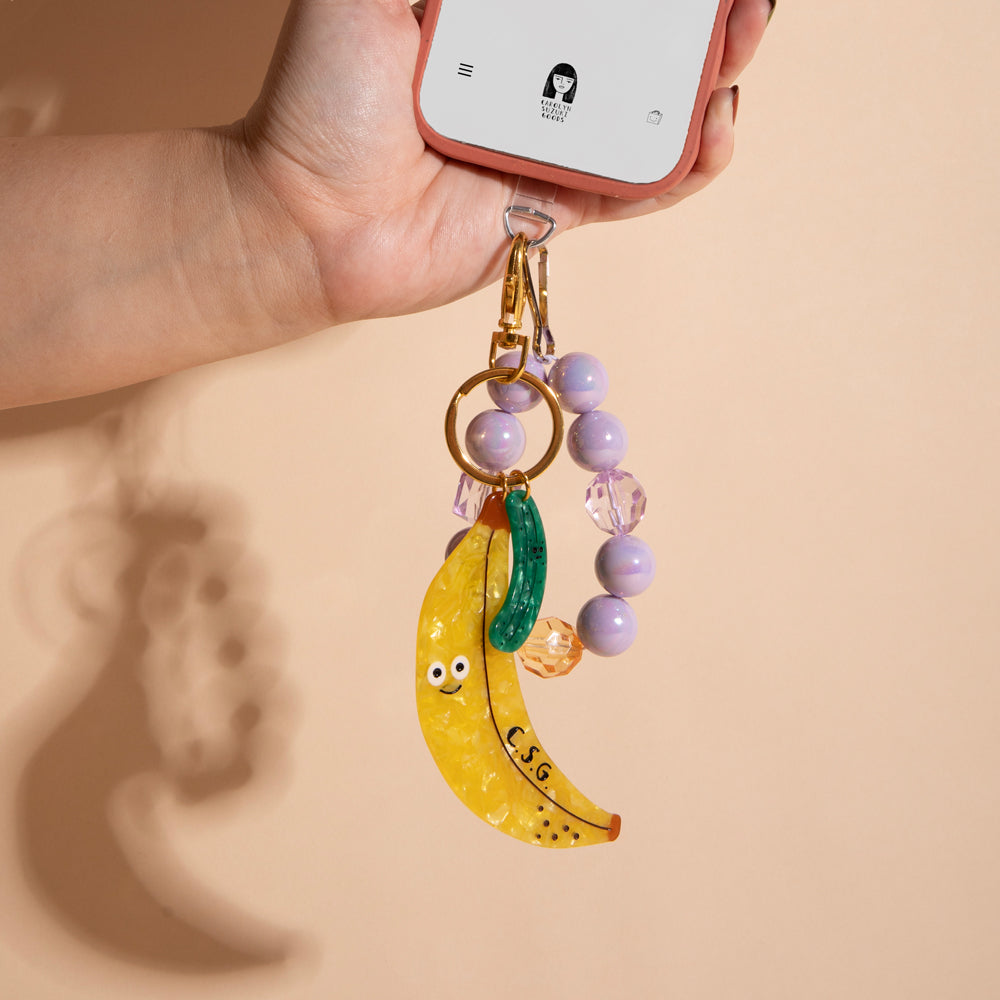 Banana-shaped keychain with a pickle on a beige background