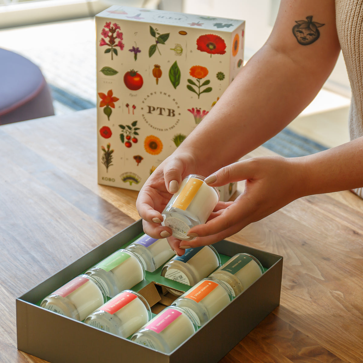 Person selecting a small container from a set of colorful containers in a box, with a PTB branded box in the background.