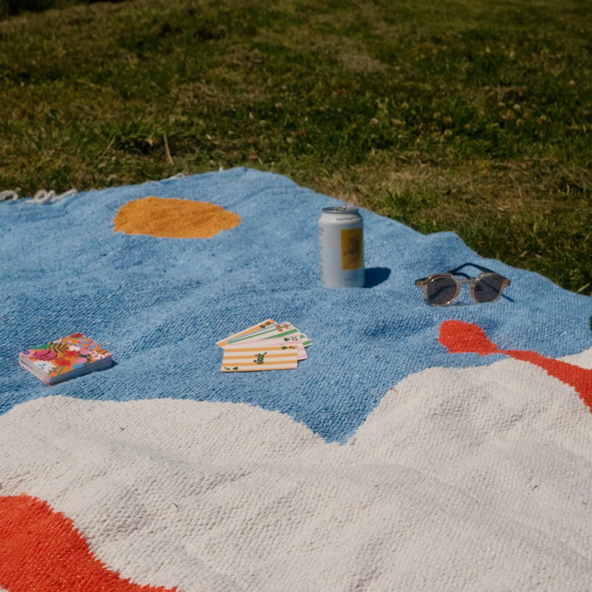 Colorful blanket with a can, sunglasses, and cards on grass