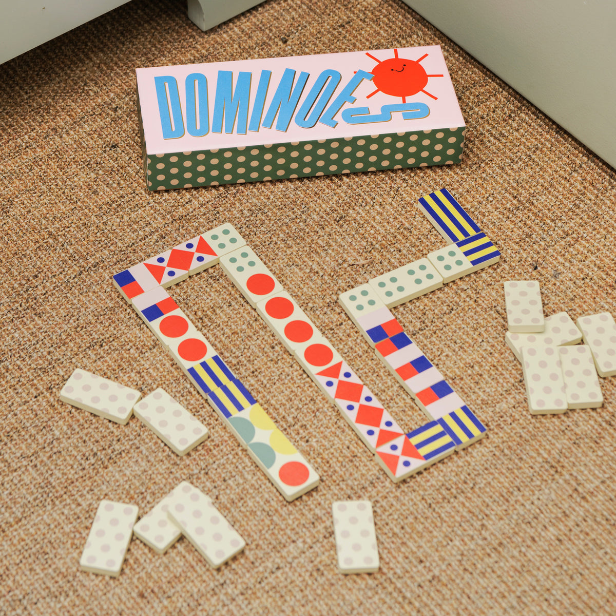 A colorful wooden domino game set shown with its illustrated storage box and several loose domino tiles on a clean white background.