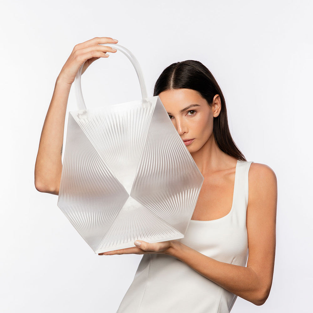 Woman holding a white, futuristic handbag against a plain background