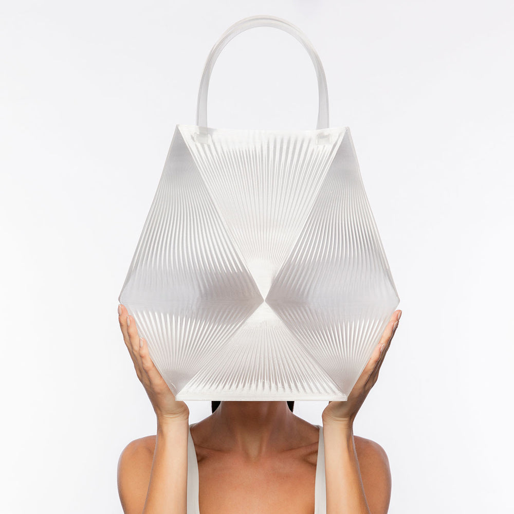 Person holding a white geometric handbag in front of their face on a white background