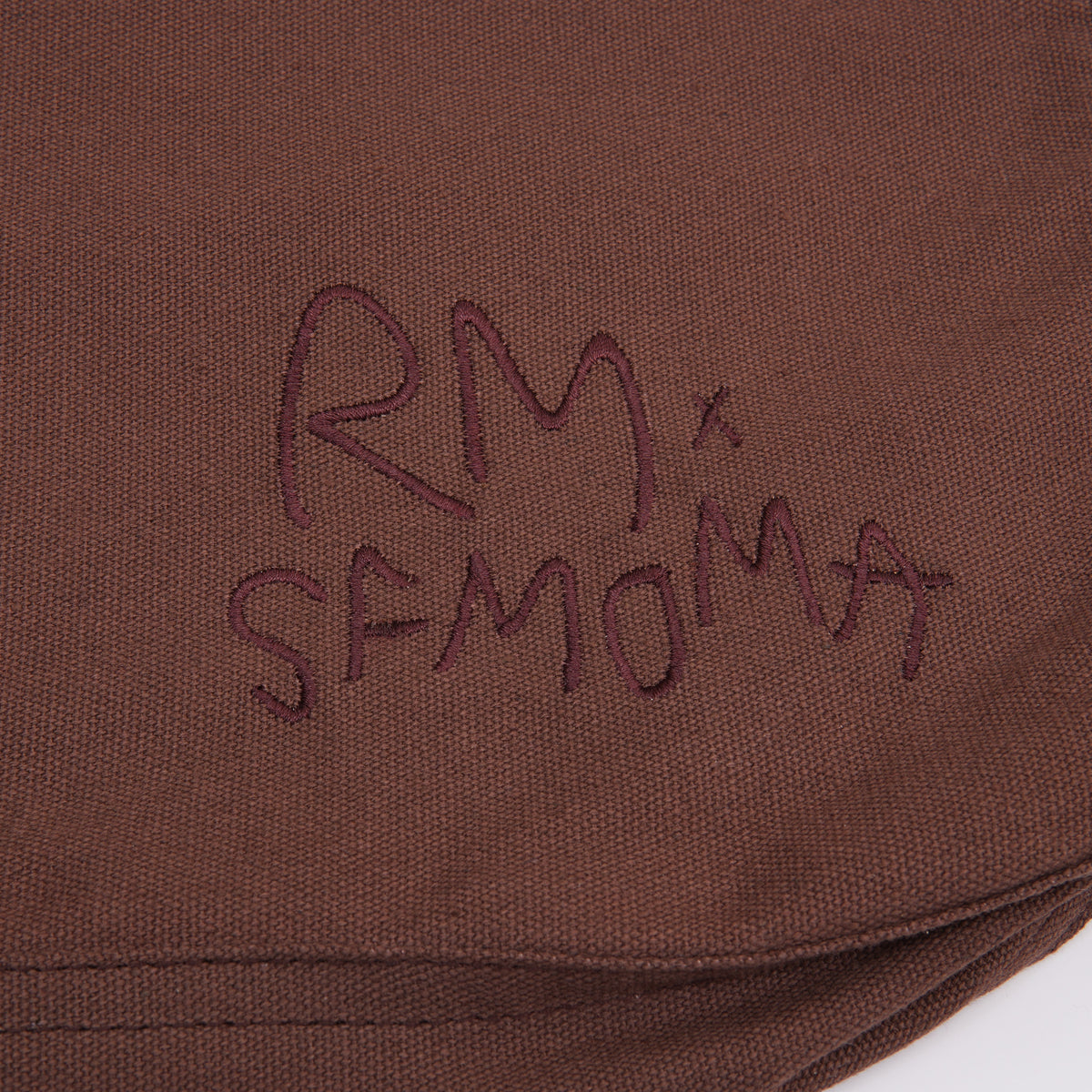Close-up of a brown fabric surface with dark embroidered script reading 'RM x SFMOMA'.