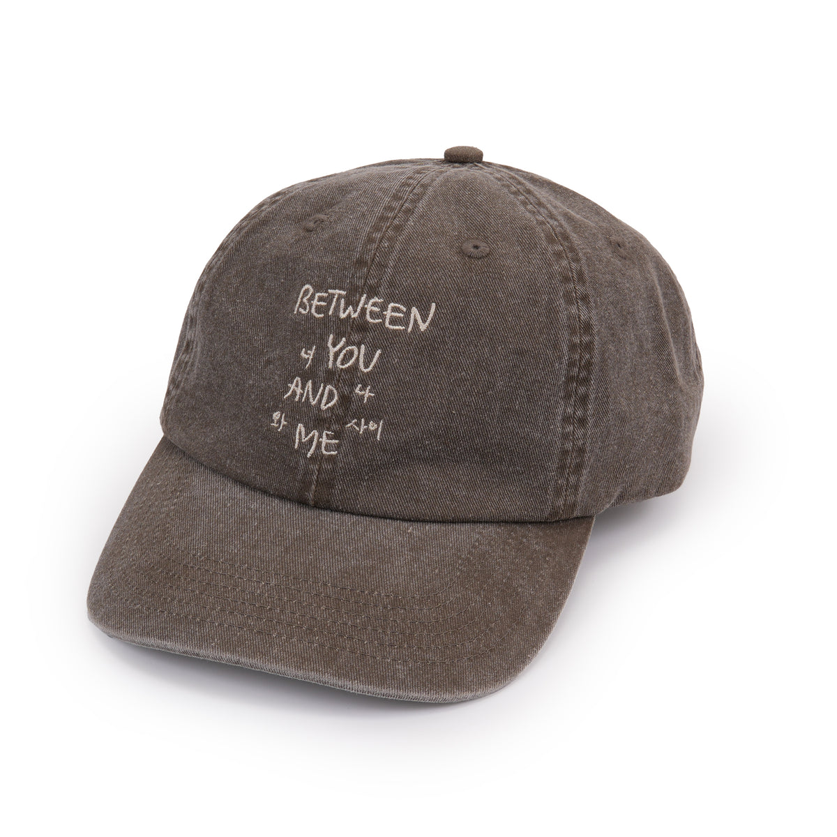 A washed dark brown baseball cap with white embroidered text reading 'BETWEEN YOU AND ME' on the front, shown on a clean white background.