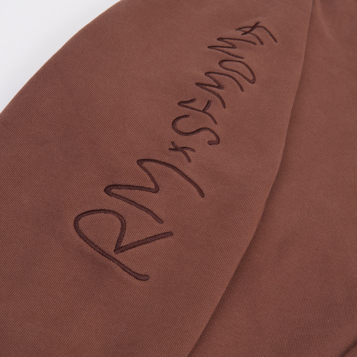 Close-up of a brown fabric surface with dark embroidered script reading 'RM x SFMOMA'.