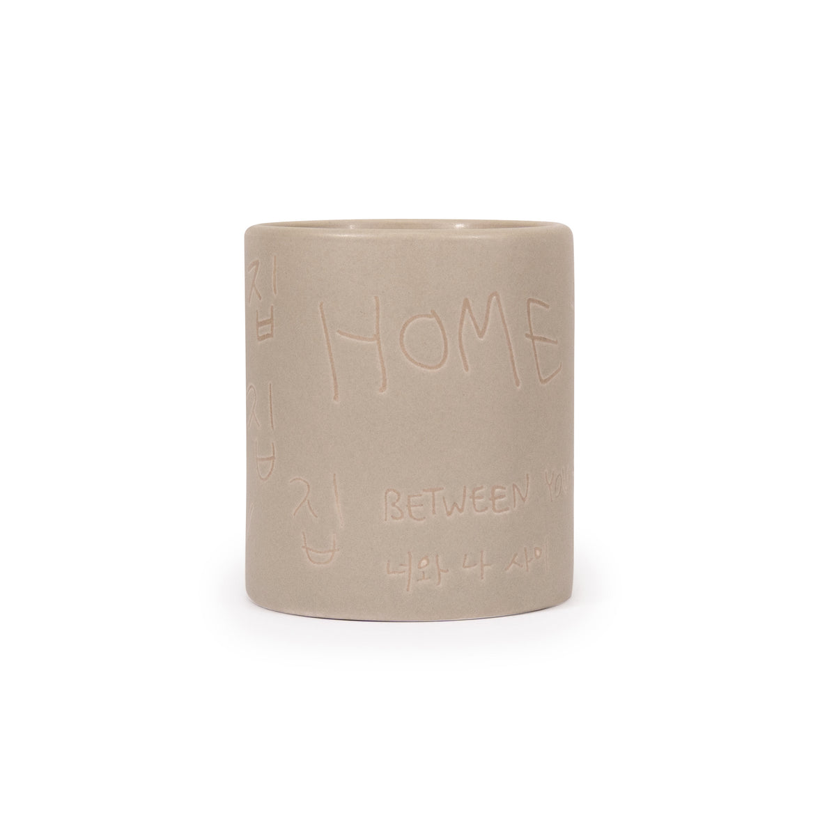 A cylindrical ceramic teacup in a matte light beige color, featuring embossed Korean text and the word 'HOME' on the front, set against a plain white background.