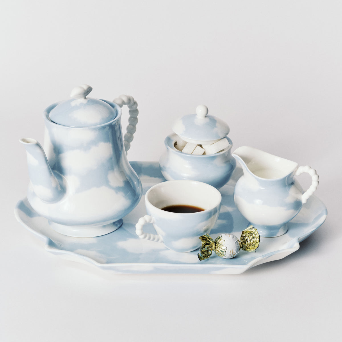 A porcelain tea and coffee set with a teapot, cup of black coffee, sugar bowl, creamer, and a decorative tray, all decorated with a light blue and white cloud pattern, set against a plain light gray background.