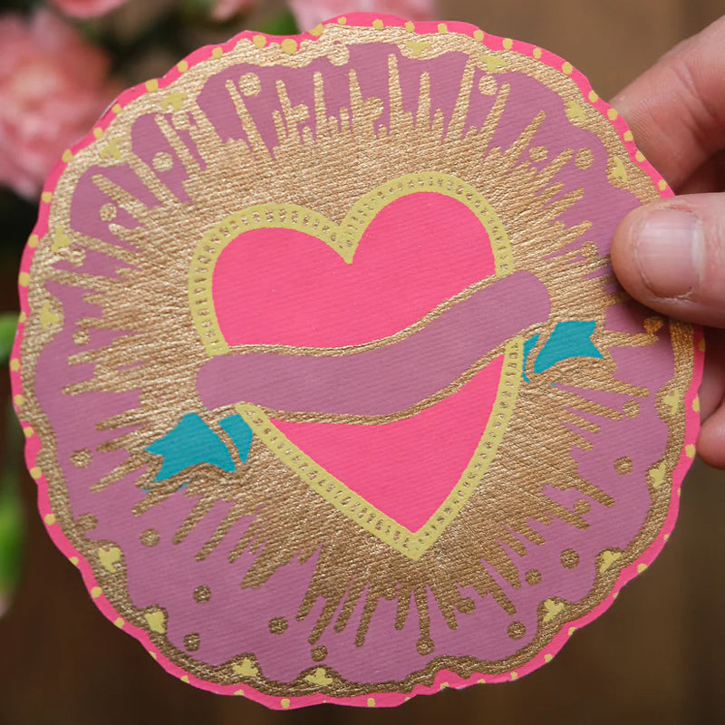 Decorative paper cutout with a heart design held by a hand against a blurred background