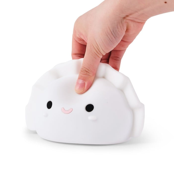 Hand pressing a cute white dumpling shaped night light with a smiling face on a white background