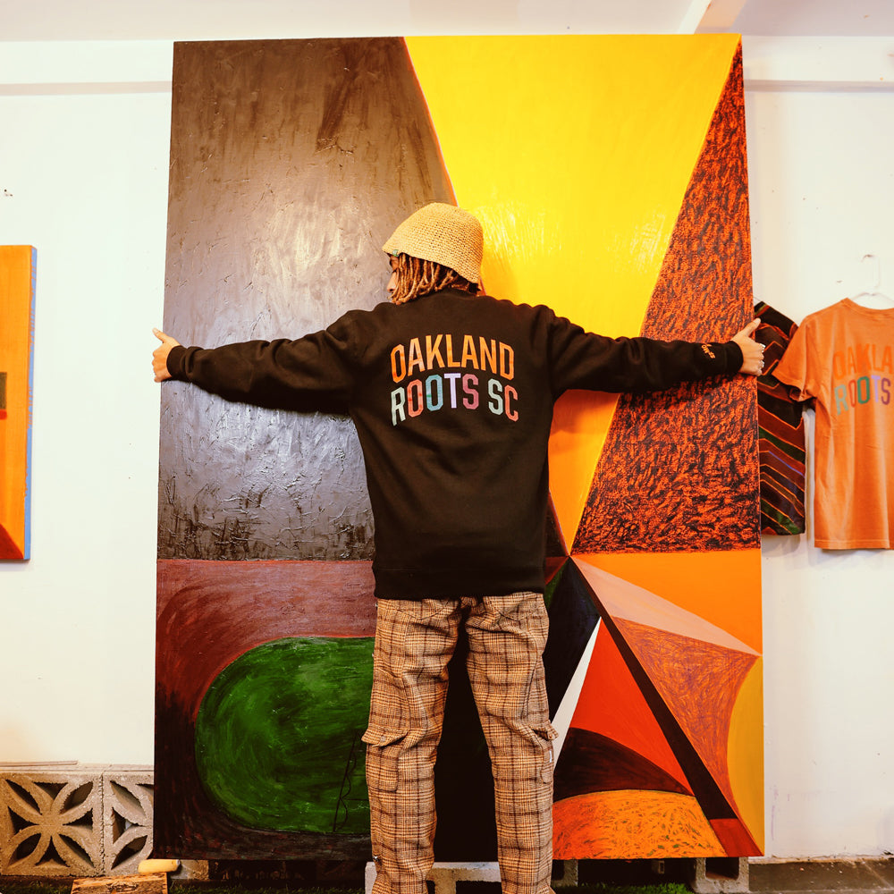 Muzae wearing sweatshirt in front of artwork.