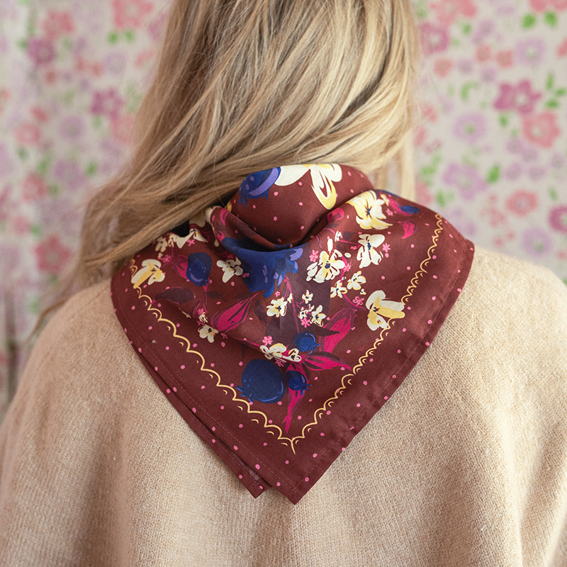 Person wearing a patterned scarf around their neck against a floral wallpaper background