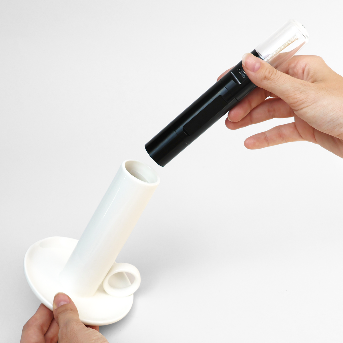 Person assembling a white and black cylindrical device on a white background