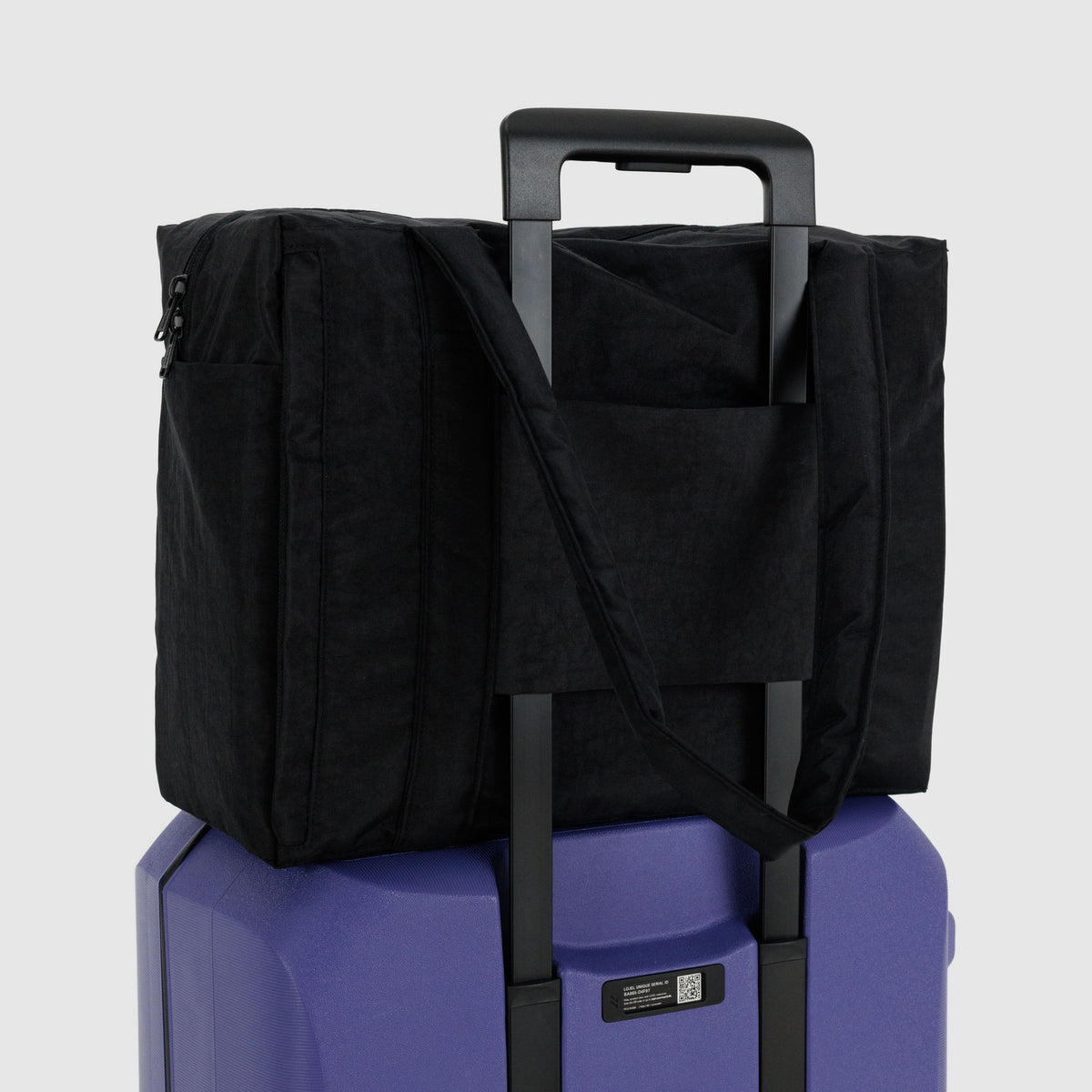 Black travel bag with shoulder strap on a blue suitcase against a light gray background