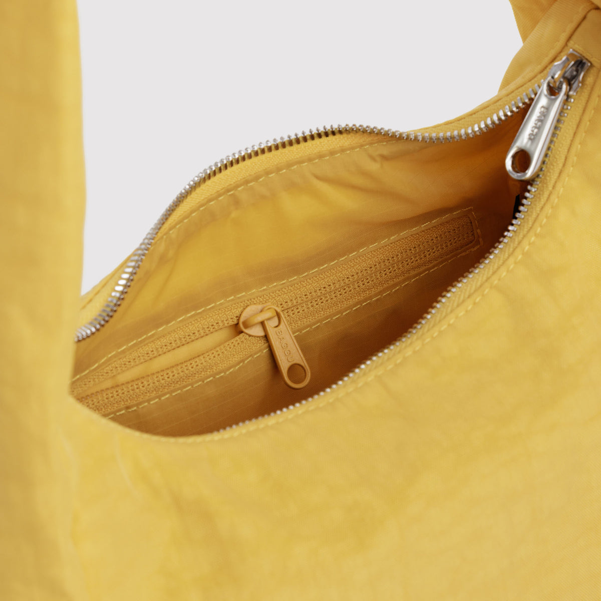 Close-up of a mustard yellow fabric bag showing the interior with a silver zipper and a matching zip pocket.