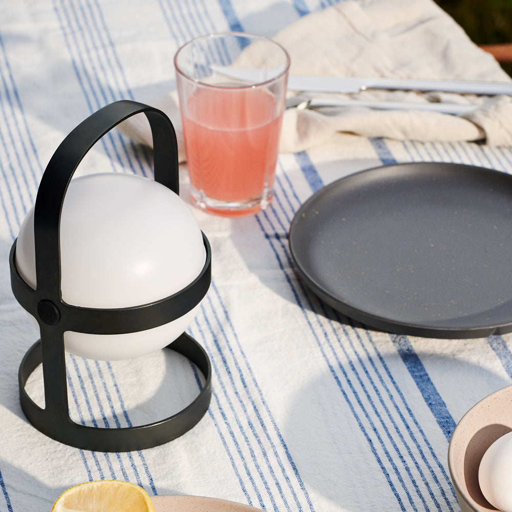 Lantern with a glass of pink drink and black plate on a striped tablecloth