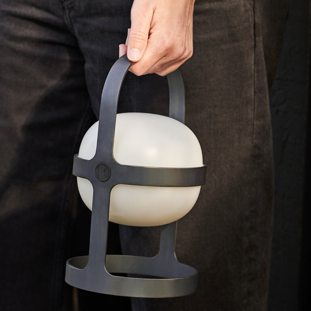 Person holding a spherical lantern with a dark handle against a dark background