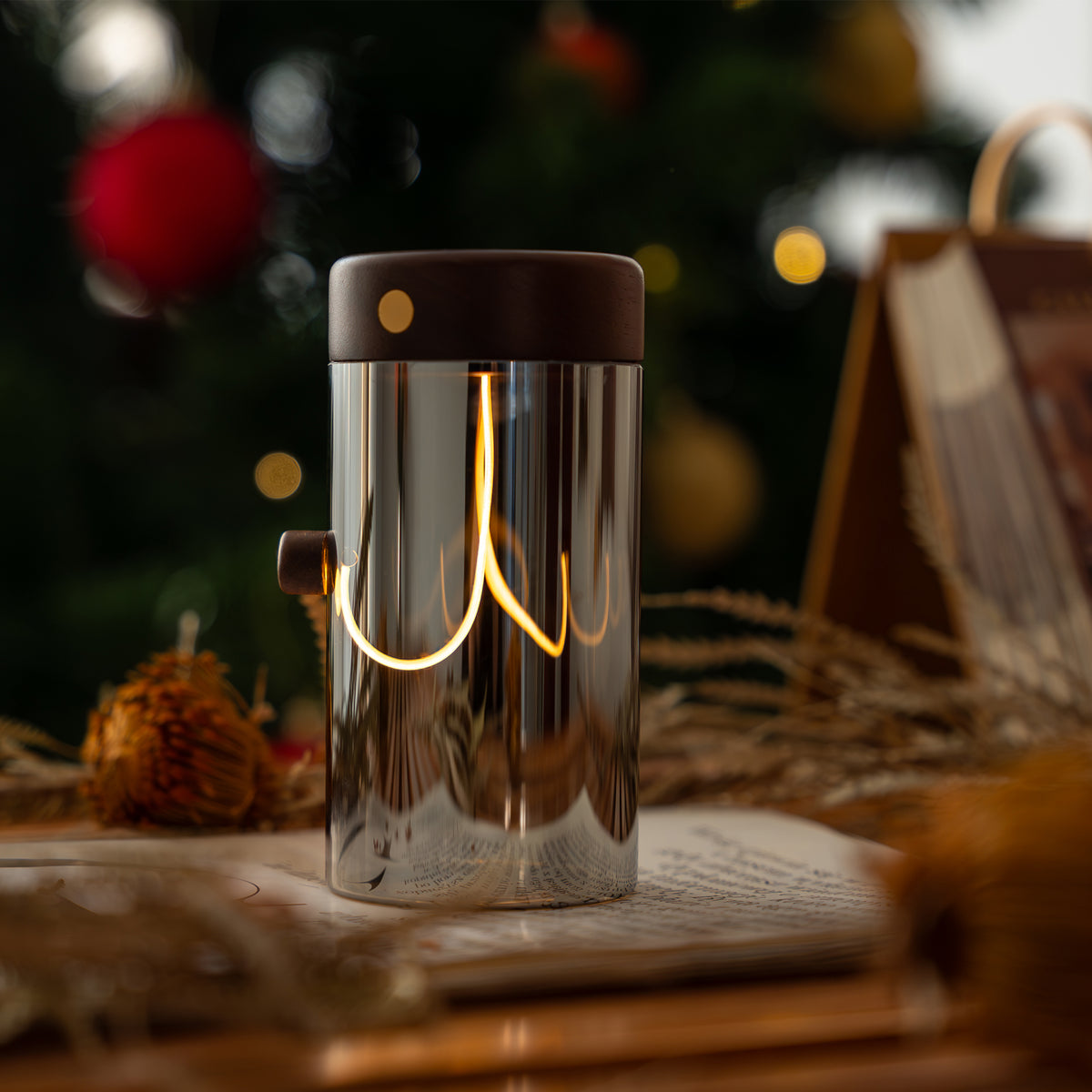 Glass lamp with a warm glow on an open book, blurred Christmas tree in the background