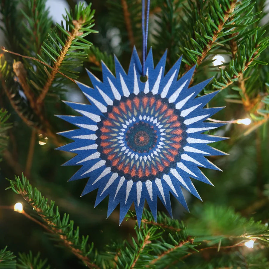 Decorative blue and orange star-shaped ornament on a Christmas tree.