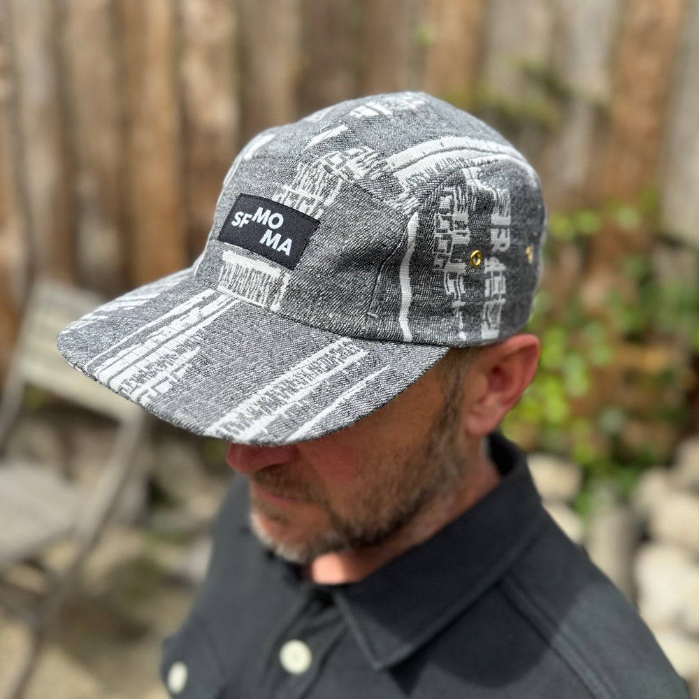 Person wearing a gray and white cap with text and patterns, outdoors.