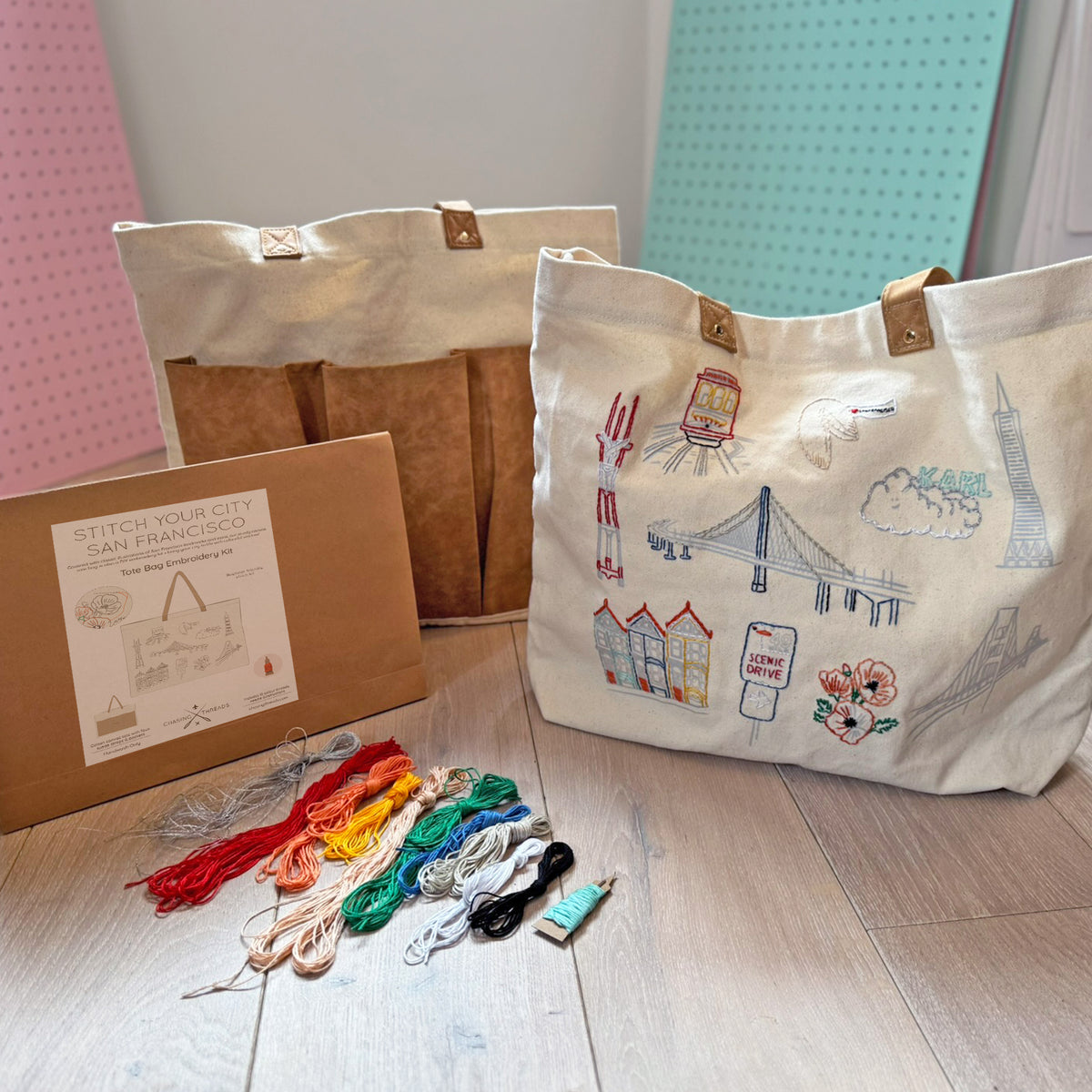 Embroidery kit with a completed tote bag featuring cityscape designs on a wooden surface.