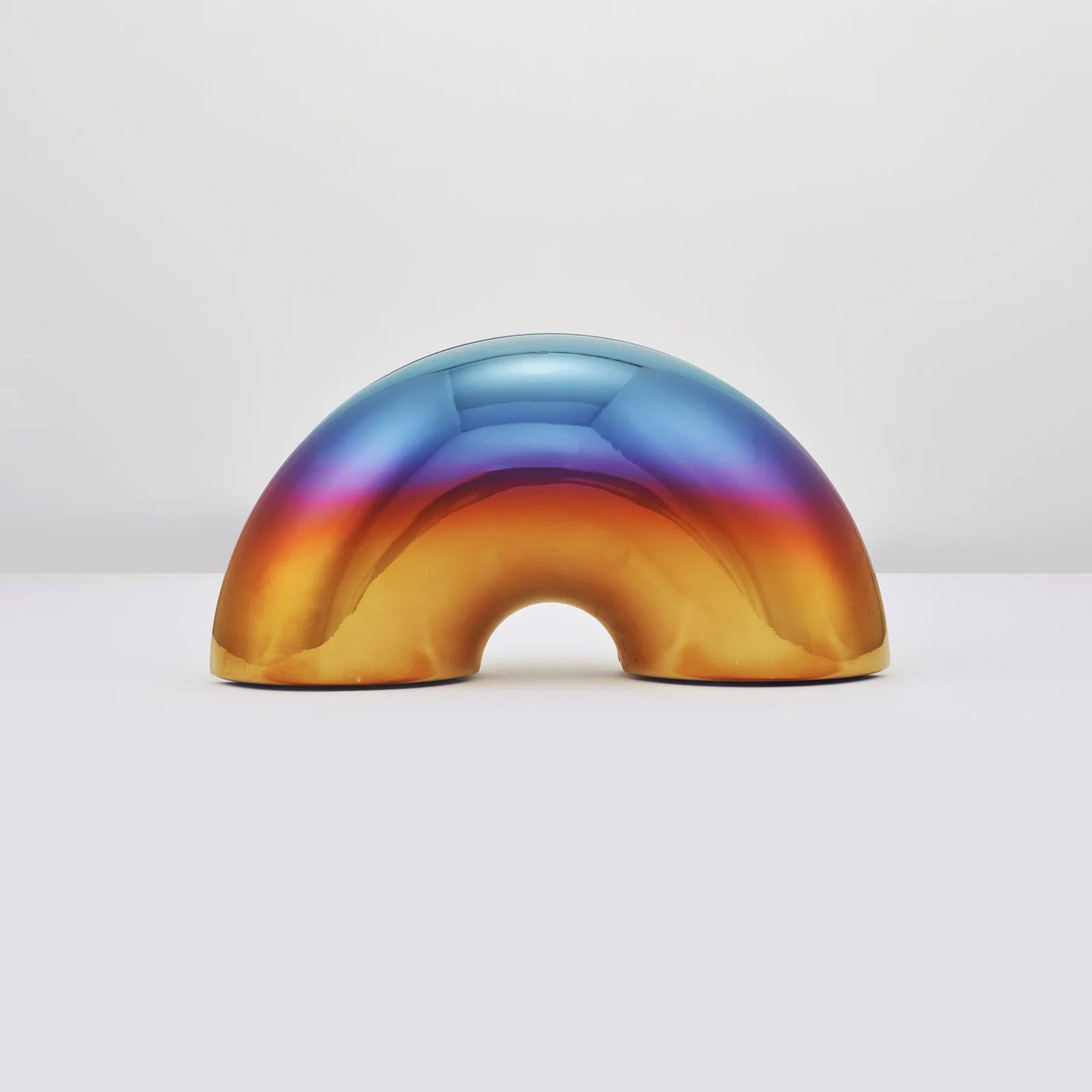 A glossy, dome-shaped menorah with a metallic rainbow finish, transitioning from blue and purple at the top to orange and gold at the bottom, displayed on a clean white surface against a light gray background.
