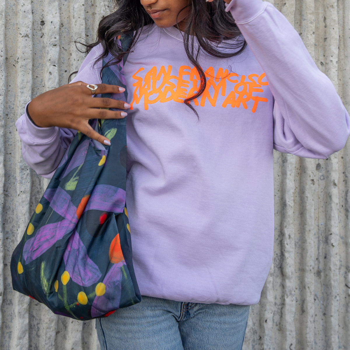 A reusable bag with a dark navy background and a colorful painted floral pattern featuring purple flowers, yellow and orange accents, and green stems.