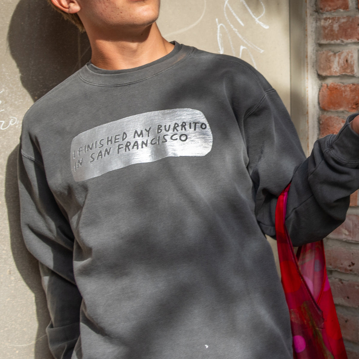 A dark gray crewneck sweatshirt with a distressed gray graphic on the chest that reads 'I FINISHED MY BURRITO IN SAN FRANCISCO' in black text.