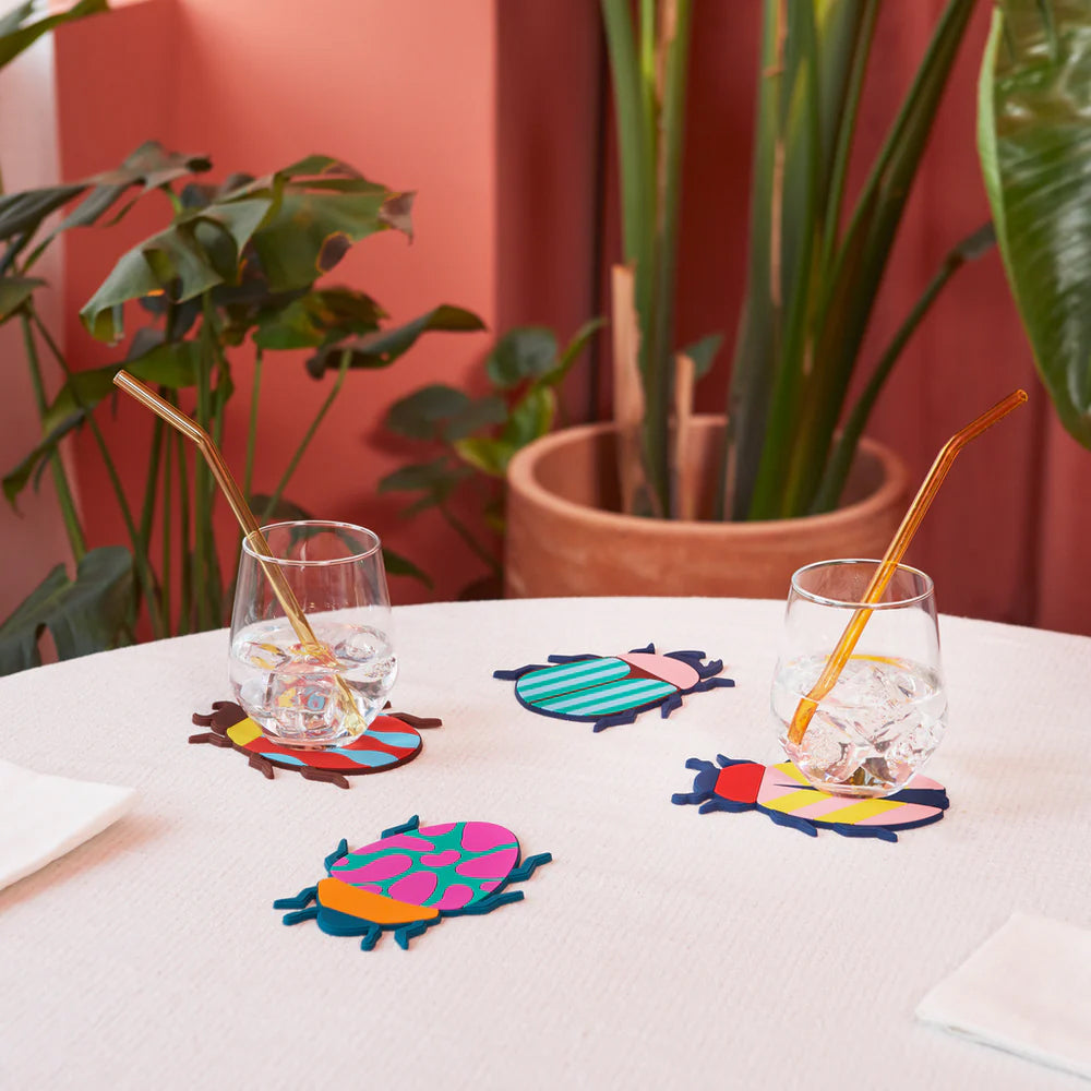 Colorful beetle-shaped coasters with a glass of orange liquid on a white background