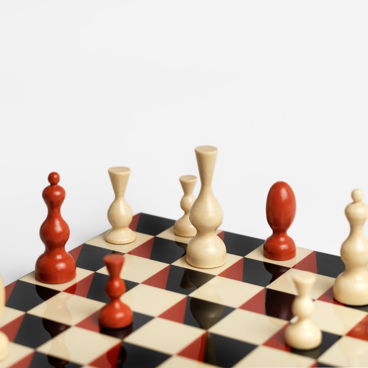 A close-up of a checkered chessboard with cream, red, and black squares, featuring several wooden chess pieces in red and cream tones on a light gray background.