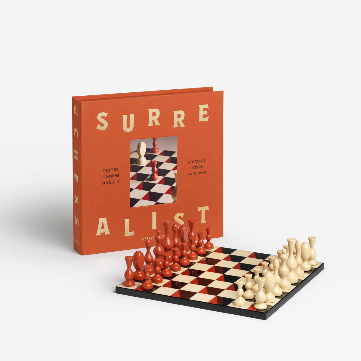 A chess set displayed in front of its orange book-style box on a clean white background. The box has large cream lettering reading 'SURREALIST' and a small inset photo of chess pieces.