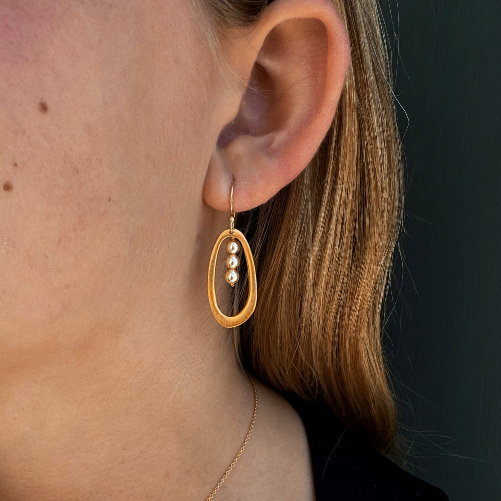 Gold oval earrings with pearl beads on a white background