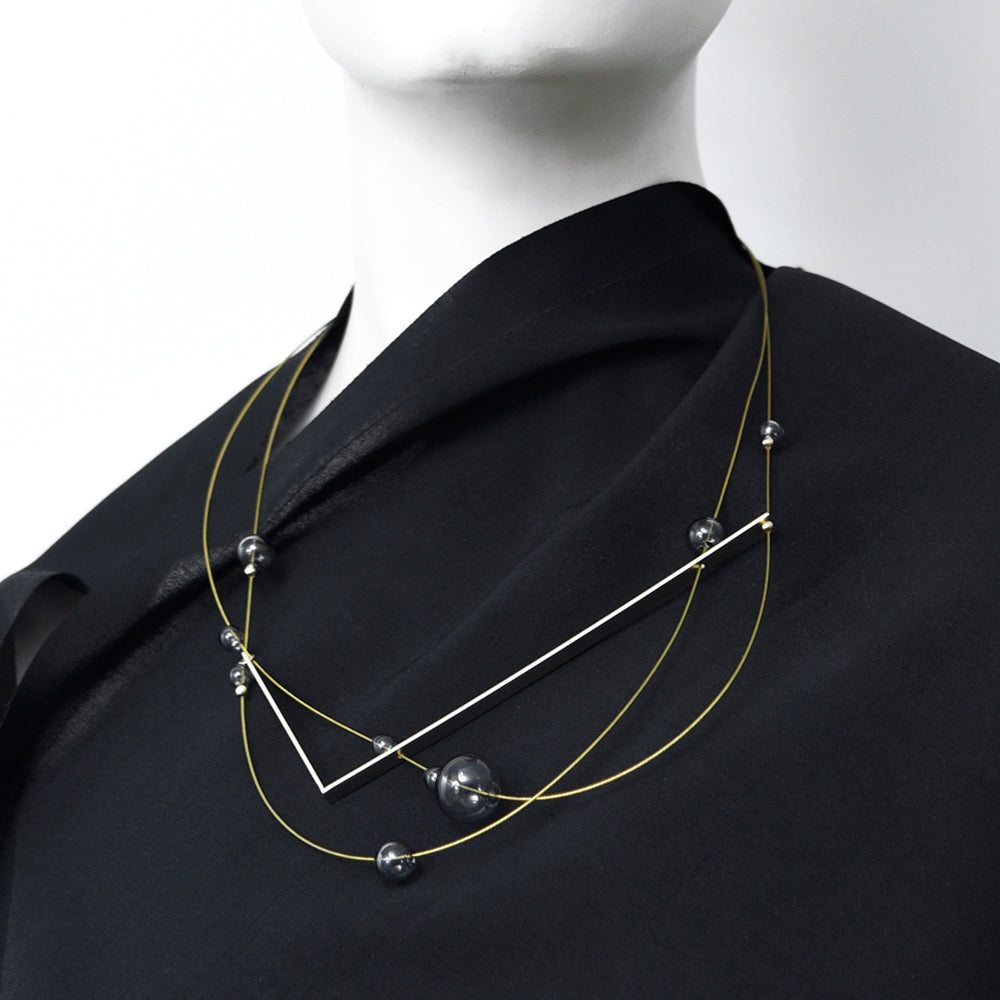 Necklace with gold bars and grey glass beads on a dark background